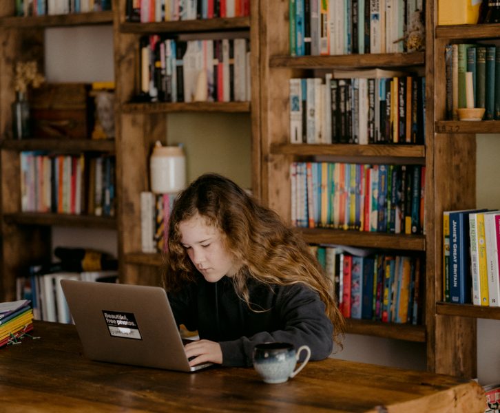 A girl looking at a computer in front of a bookshelf