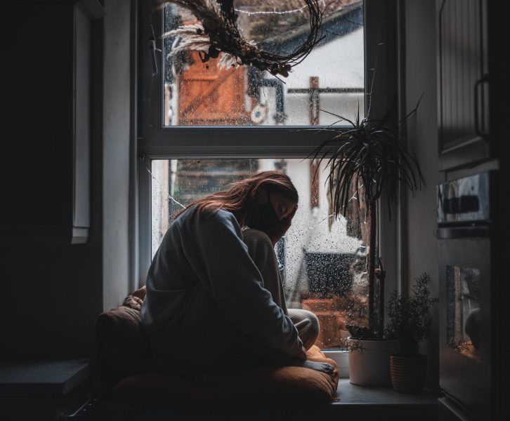 girl sitting in dark window wearing a mask