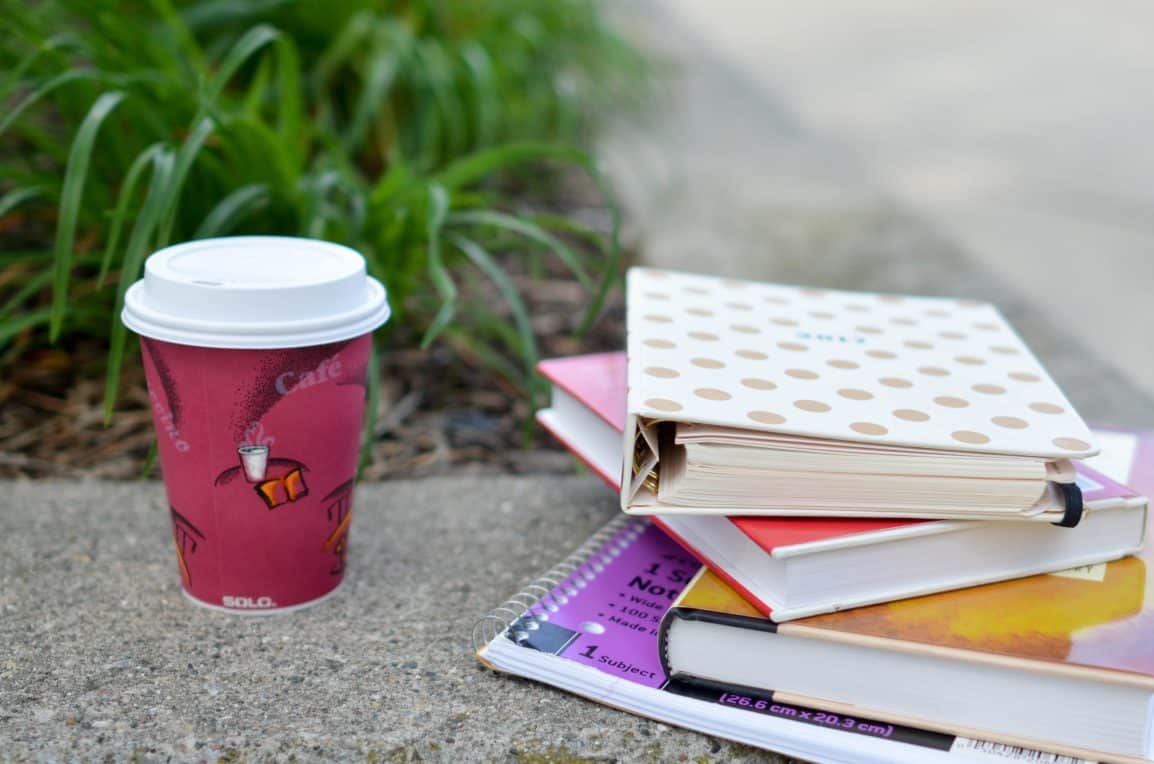 school notebooks and textbooks resting on a concrete bench accompanied by a coffee