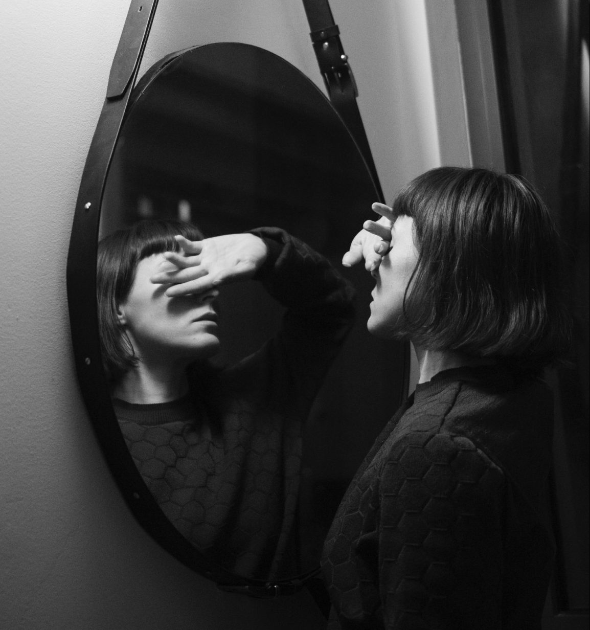 A woman stands in front of a mirror and covers her eyes