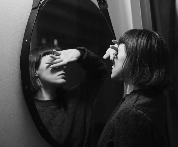 A woman stands in front of a mirror and covers her eyes