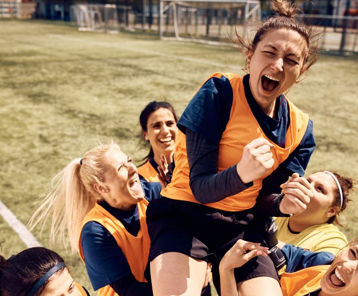 6 girls in a field outside doing activities. Wearing orange and black clothing.